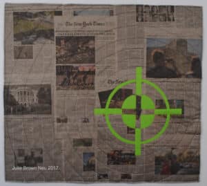 art quilt of newspaper headlines from Las Vegas Shooting, overlaid with green gun sight image
