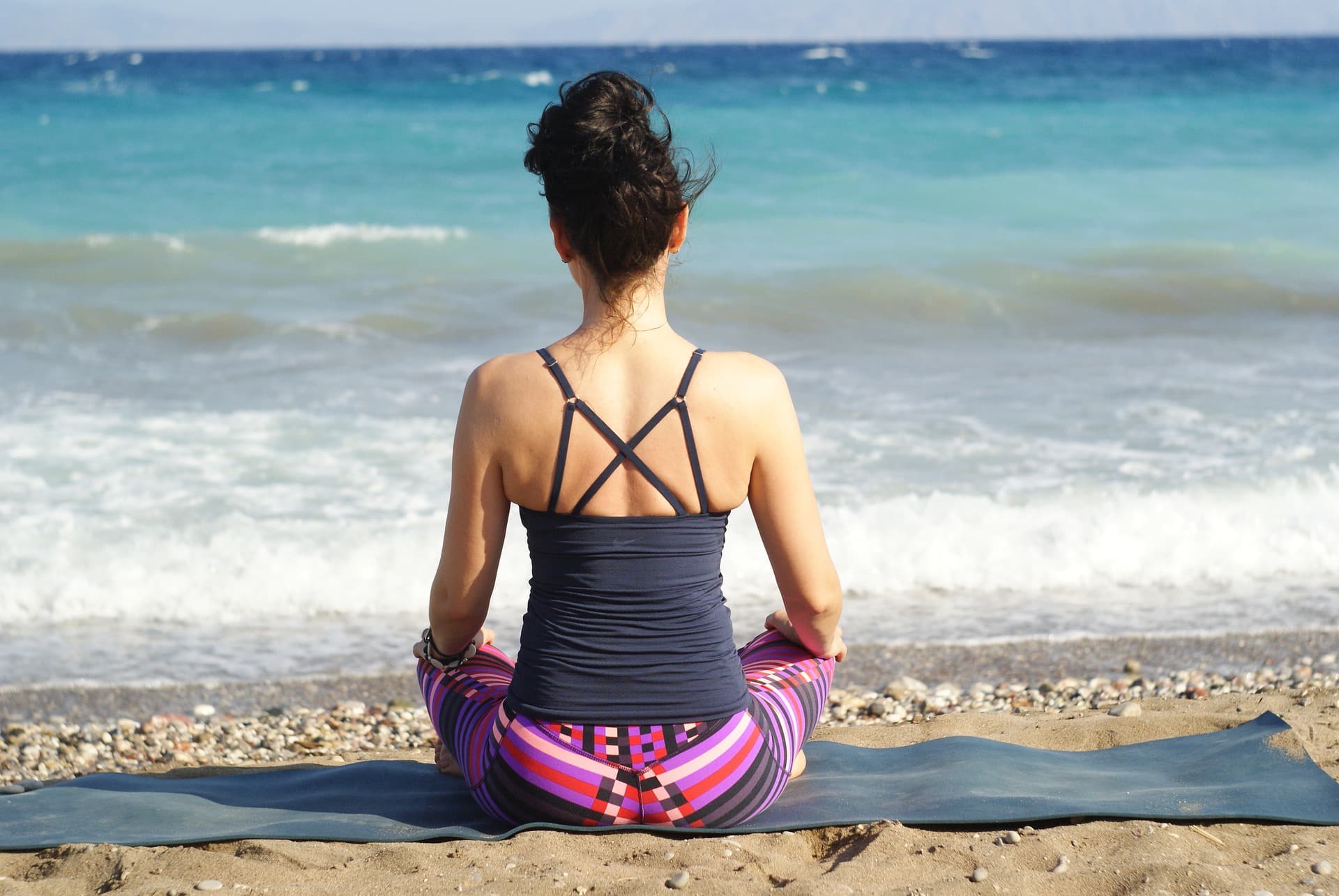 meditating woman on beach, facing gentle waves