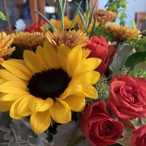 close up image of fall flower bouquet with sunflowers and orange roses