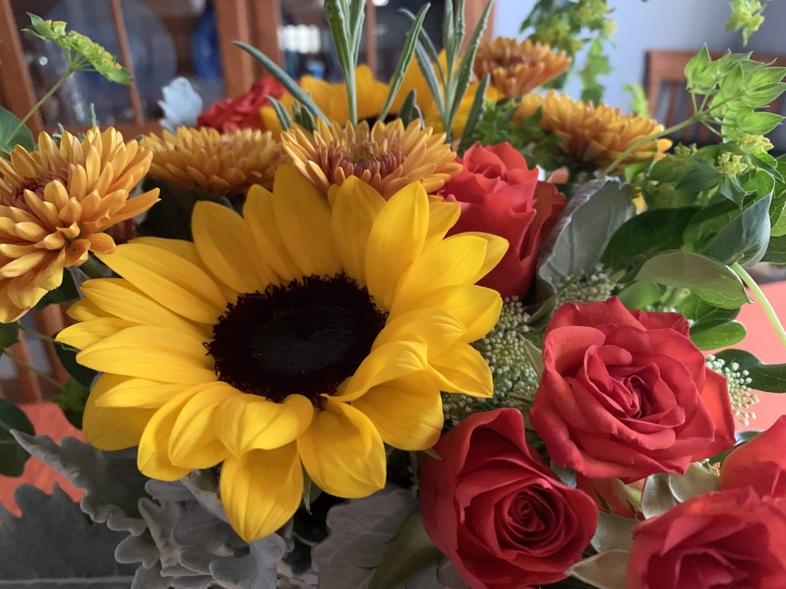 close up image of fall flower bouquet with sunflowers and orange roses
