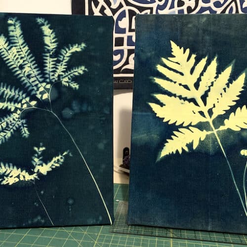 two cyanotypes of light yellow fern leaves on deep blue backgrounds, stretched over canvases and propped on tabletop