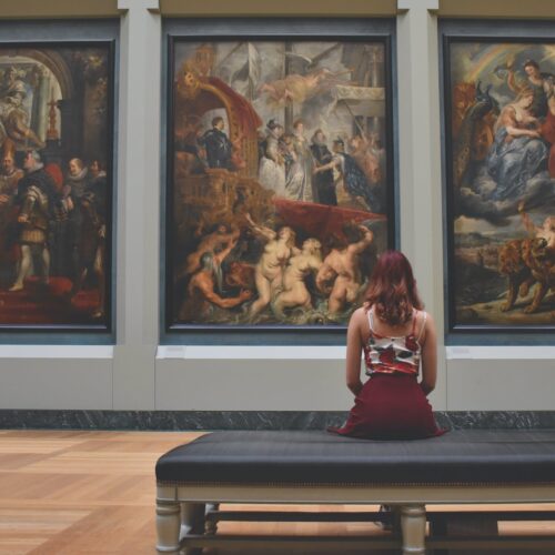 woman sitting on ottoman in front of three paintings